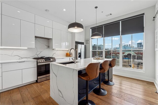 kitchen featuring gas stove, white cabinetry, light stone counters, light wood-type flooring, and decorative backsplash