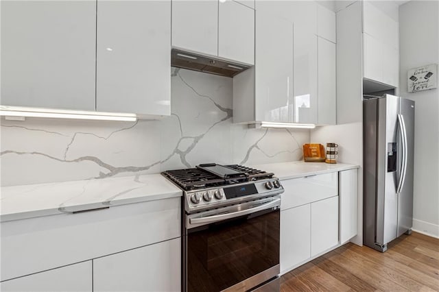 kitchen featuring appliances with stainless steel finishes, light stone counters, tasteful backsplash, white cabinets, and light wood-type flooring