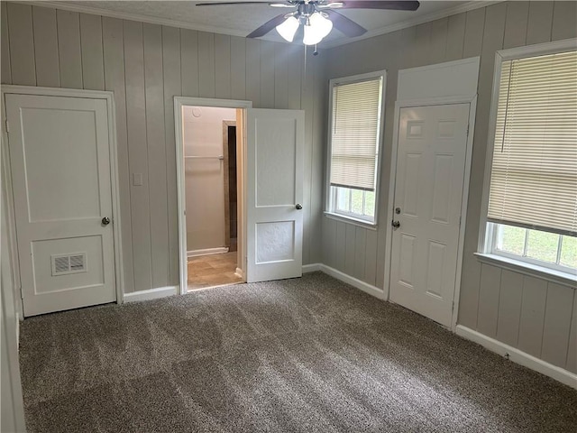 unfurnished bedroom featuring crown molding, carpet floors, multiple windows, baseboards, and wooden walls