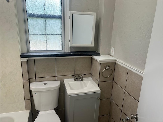 bathroom with tile walls, toilet, vanity, a textured wall, and a wainscoted wall