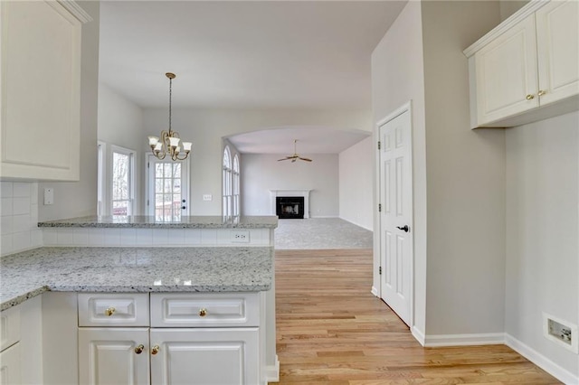 kitchen with light stone counters, kitchen peninsula, light hardwood / wood-style floors, ceiling fan with notable chandelier, and white cabinets