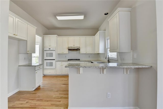 kitchen with white cabinets, a breakfast bar, kitchen peninsula, and double oven