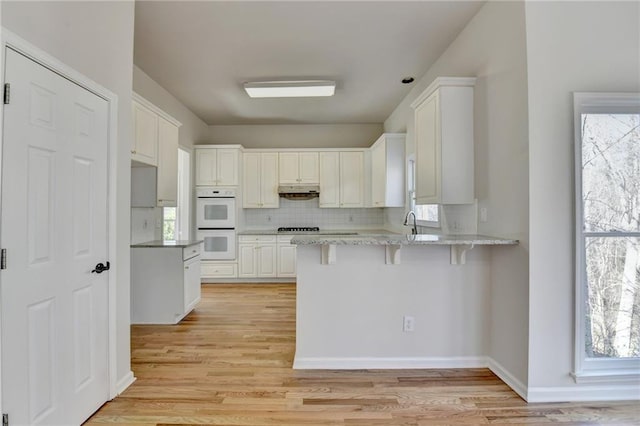 kitchen with white cabinets, light stone counters, a kitchen breakfast bar, kitchen peninsula, and decorative backsplash