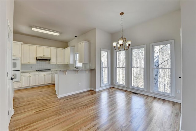 kitchen with kitchen peninsula, gas stovetop, decorative backsplash, and white cabinetry