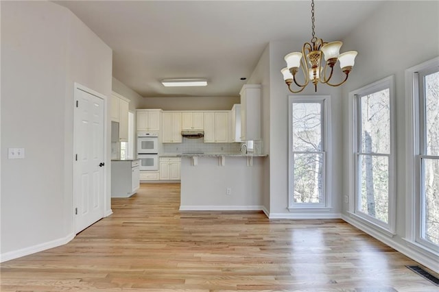 kitchen with white double oven, light hardwood / wood-style floors, decorative backsplash, an inviting chandelier, and white cabinets