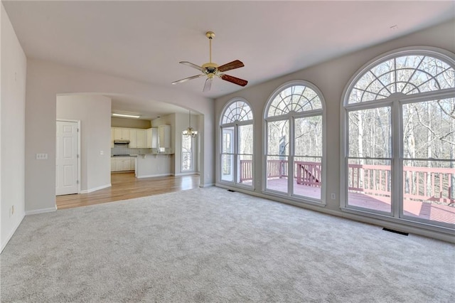 unfurnished living room featuring ceiling fan with notable chandelier and light colored carpet