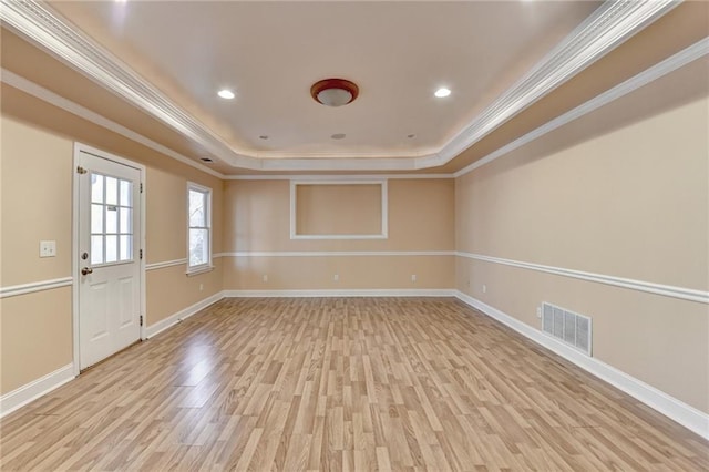 spare room with light wood-type flooring, a tray ceiling, and crown molding