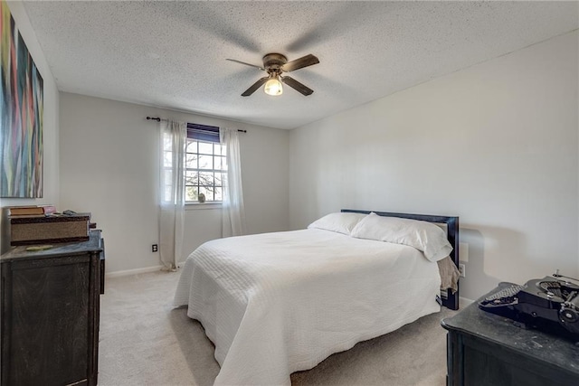 bedroom featuring light carpet, ceiling fan, baseboards, and a textured ceiling