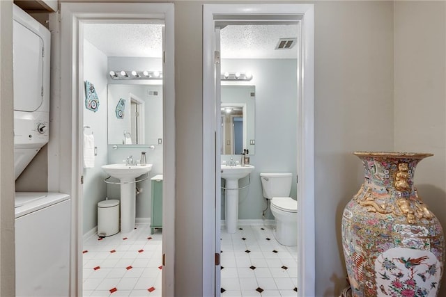 half bath with a sink, a textured ceiling, visible vents, and stacked washer / drying machine