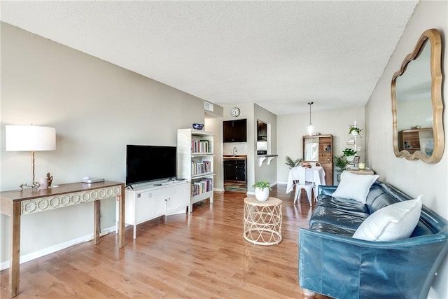 living area featuring a textured ceiling, baseboards, visible vents, and light wood-style floors