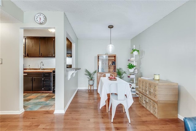 dining room with a textured ceiling, light wood-style flooring, and baseboards