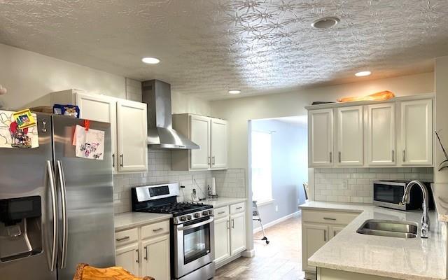 kitchen featuring appliances with stainless steel finishes, sink, wall chimney range hood, and white cabinetry