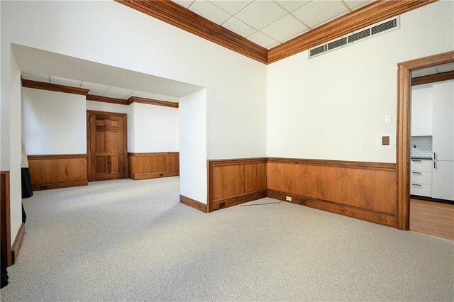 carpeted empty room featuring a drop ceiling and crown molding