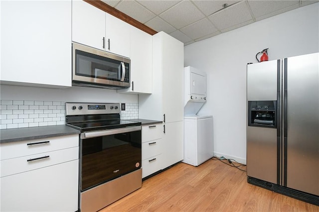 kitchen with stainless steel appliances, dark countertops, white cabinets, and stacked washer / drying machine