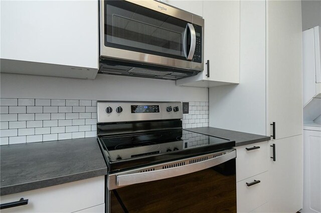 kitchen featuring stacked washing maching and dryer, white cabinets, decorative backsplash, and stainless steel appliances