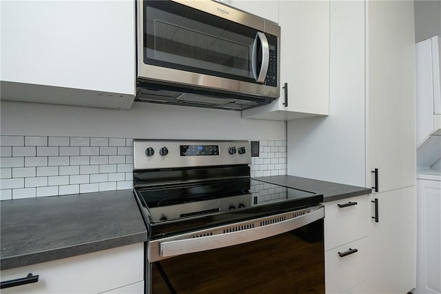 kitchen with white cabinets, dark countertops, stainless steel appliances, and backsplash