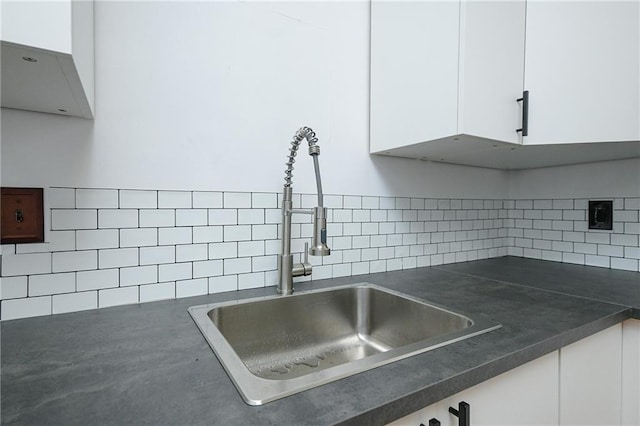 interior details featuring dark countertops, white cabinets, a sink, and decorative backsplash