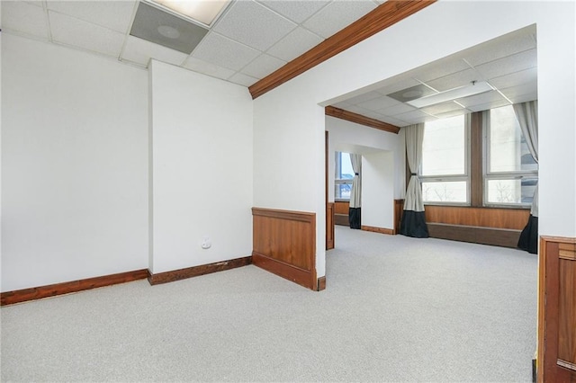 spare room featuring light carpet, a drop ceiling, and baseboards