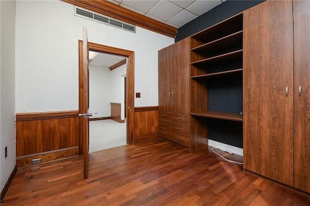 unfurnished bedroom with dark wood-style flooring, a wainscoted wall, visible vents, wood walls, and a drop ceiling