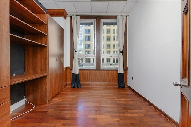 spare room featuring a drop ceiling, dark wood finished floors, and baseboards