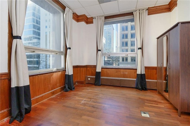 spare room featuring a paneled ceiling, wooden walls, a wainscoted wall, wood finished floors, and crown molding