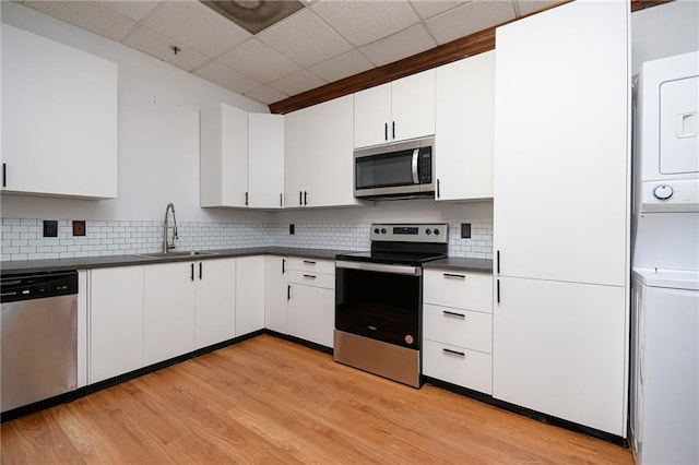 kitchen featuring dark countertops, appliances with stainless steel finishes, white cabinetry, a sink, and stacked washing maching and dryer