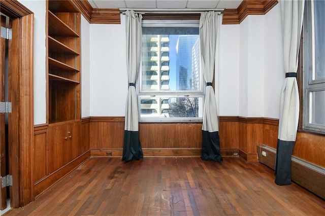 spare room with dark wood-style floors, wainscoting, ornamental molding, and wood walls