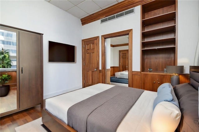 bedroom with a wainscoted wall, visible vents, light wood-style floors, ornamental molding, and a drop ceiling