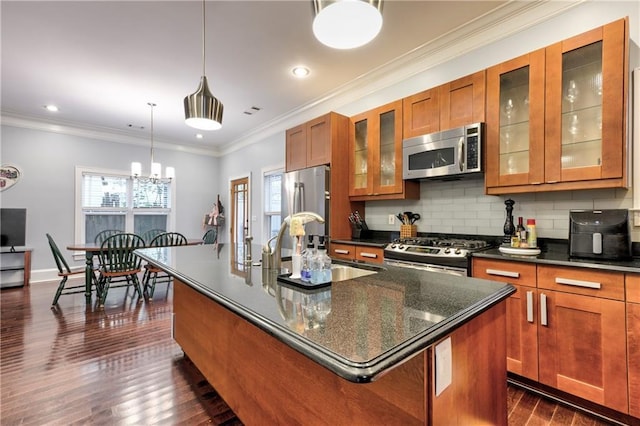 kitchen featuring pendant lighting, ornamental molding, appliances with stainless steel finishes, and a kitchen island with sink