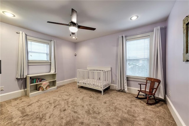 carpeted bedroom featuring a nursery area and ceiling fan