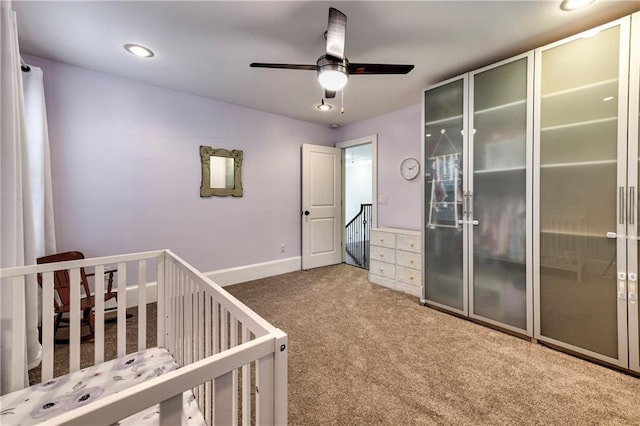 unfurnished bedroom with a nursery area, ceiling fan, and carpet