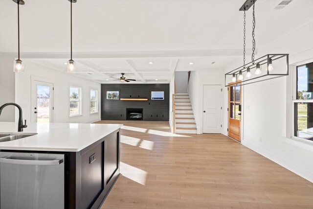 kitchen featuring light wood-style flooring, a large fireplace, coffered ceiling, a sink, and stainless steel dishwasher