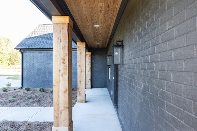 entrance to property featuring a shingled roof and brick siding