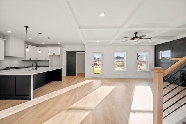 kitchen featuring light wood finished floors, a barn door, white cabinets, a sink, and coffered ceiling