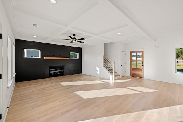 unfurnished living room featuring light wood-type flooring, coffered ceiling, beamed ceiling, and stairway