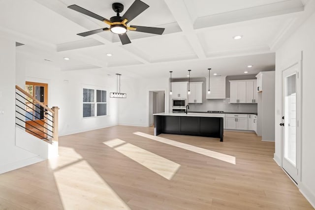 kitchen with stainless steel microwave, white cabinetry, light wood-type flooring, coffered ceiling, and beamed ceiling