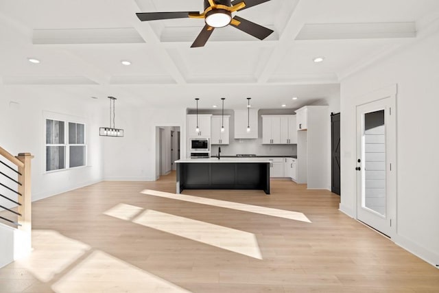 kitchen with light wood-style flooring, a kitchen island with sink, built in microwave, and white cabinets