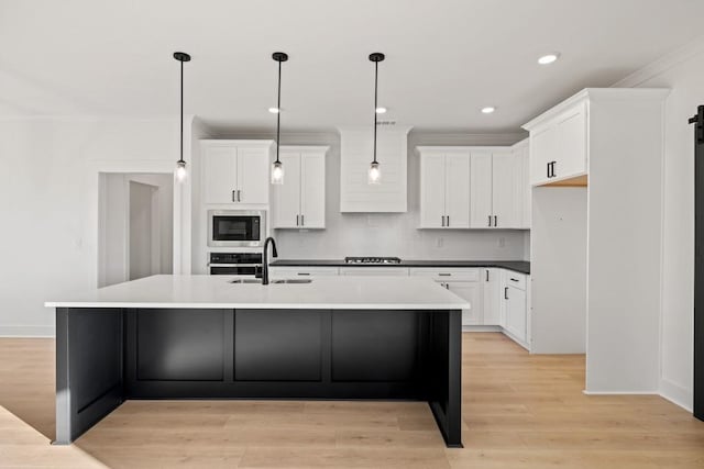 kitchen featuring stainless steel appliances, white cabinets, a sink, and an island with sink