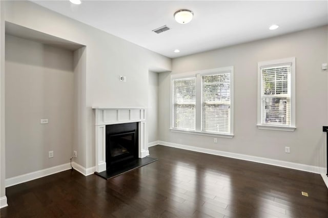 unfurnished living room with baseboards, visible vents, dark wood finished floors, recessed lighting, and a glass covered fireplace