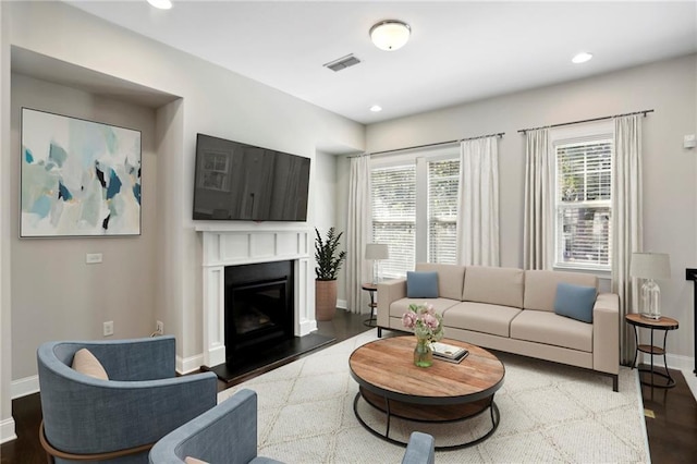 living room with visible vents, a glass covered fireplace, wood finished floors, recessed lighting, and baseboards