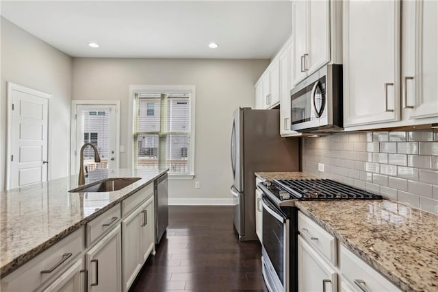 kitchen with dark wood-style floors, light stone countertops, a sink, stainless steel appliances, and tasteful backsplash