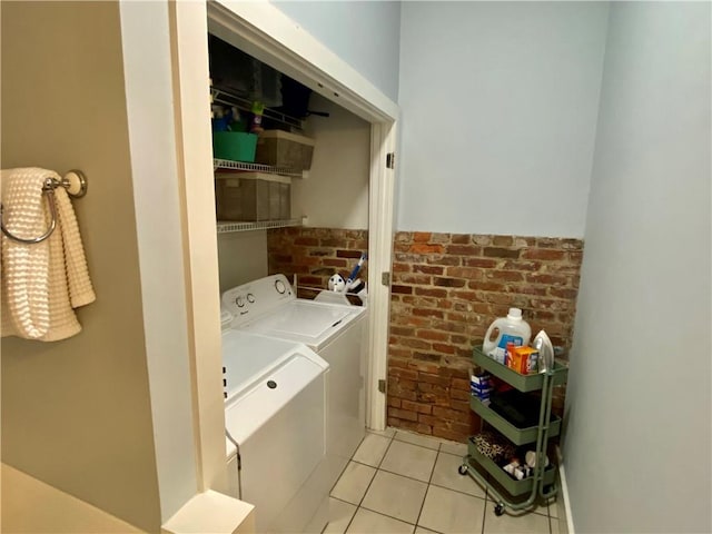 clothes washing area with brick wall, washer and clothes dryer, and light tile patterned flooring