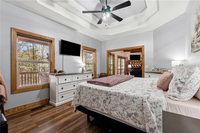 bedroom featuring a raised ceiling, multiple windows, ceiling fan, and dark hardwood / wood-style flooring