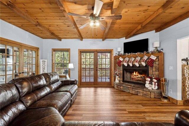 living room featuring french doors, wood ceiling, beam ceiling, hardwood / wood-style floors, and a stone fireplace