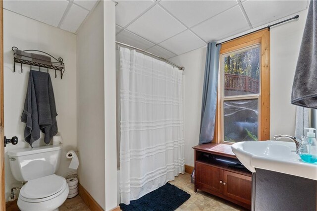 bathroom with a shower with shower curtain, a drop ceiling, toilet, and vanity