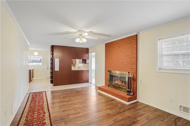 unfurnished living room featuring a brick fireplace, crown molding, hardwood / wood-style floors, and ceiling fan