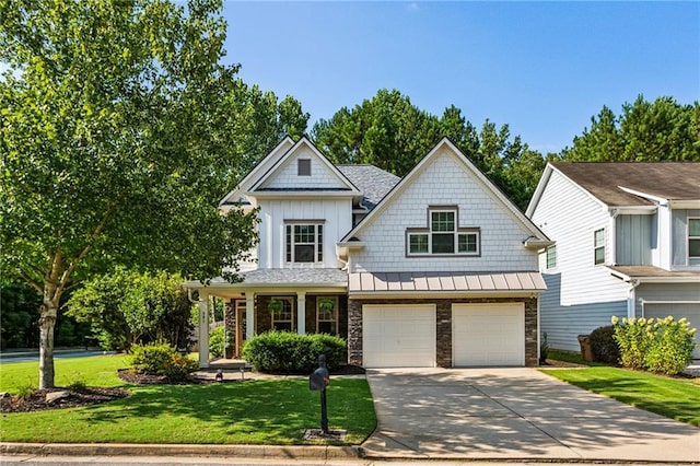 view of front of house with a front lawn, stone siding, a standing seam roof, an attached garage, and driveway