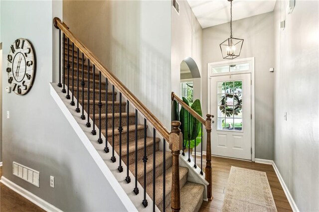 entrance foyer with a notable chandelier, stairs, baseboards, dark wood-type flooring, and visible vents