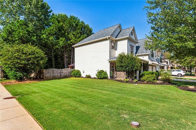 view of side of property featuring fence, a lawn, and roof with shingles