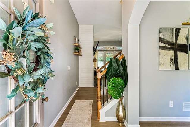 corridor featuring arched walkways, stairs, baseboards, wood finished floors, and visible vents